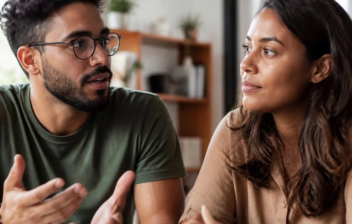 Duas pessoas sentadas de frente uma para a outra à mesa: uma fala, a outra registra por escrito